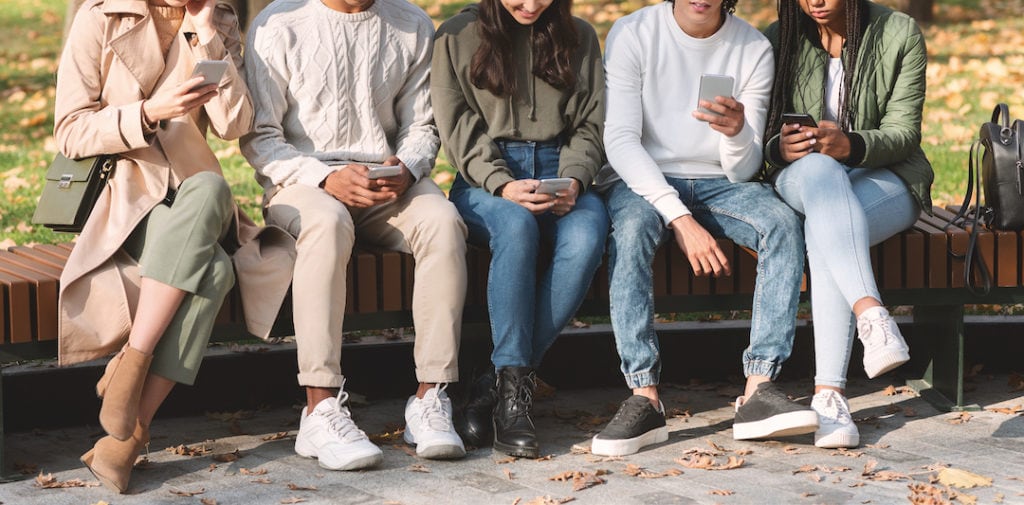 Social Media Kanäle: Eine Gruppe internationaler Social Media Kanäle: Jugendlicher mit Smartphones in einem Park, die sich Twitter-Nachrichten ansehen.