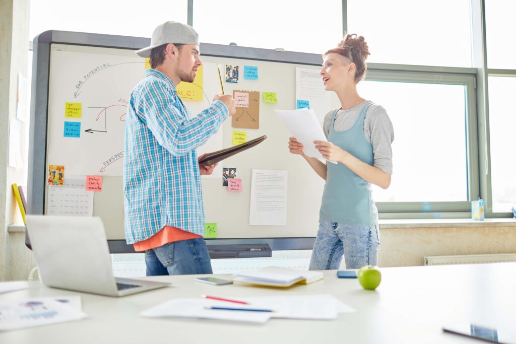 Ein selbstbewusstes, kreatives Marketingteam in legerer Kleidung geht Papiere und Notizen durch, während es im Büro ein Brainstorming zu Content Marketing Strategien durchführt und an einem neuen Projekt arbeitet