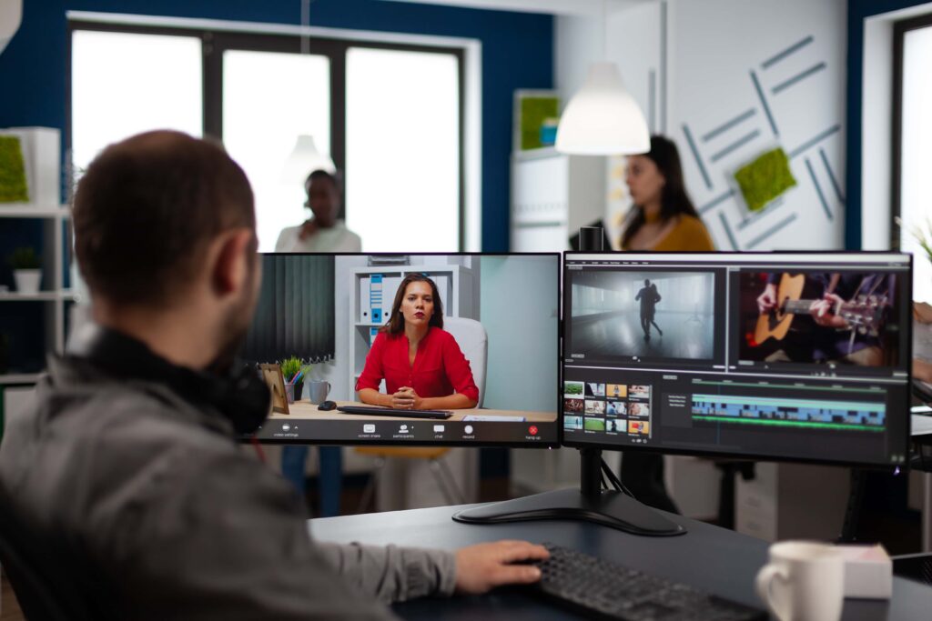 Video Produktion: Video-Editor in Web-Online-Produktionskonferenz mit Projektleiter per Videoanruf, Bearbeitung von Kundenarbeiten, Einholen von Feedback zu Unternehmensfilmen mit Postproduktionssoftware auf zwei Monitoren.