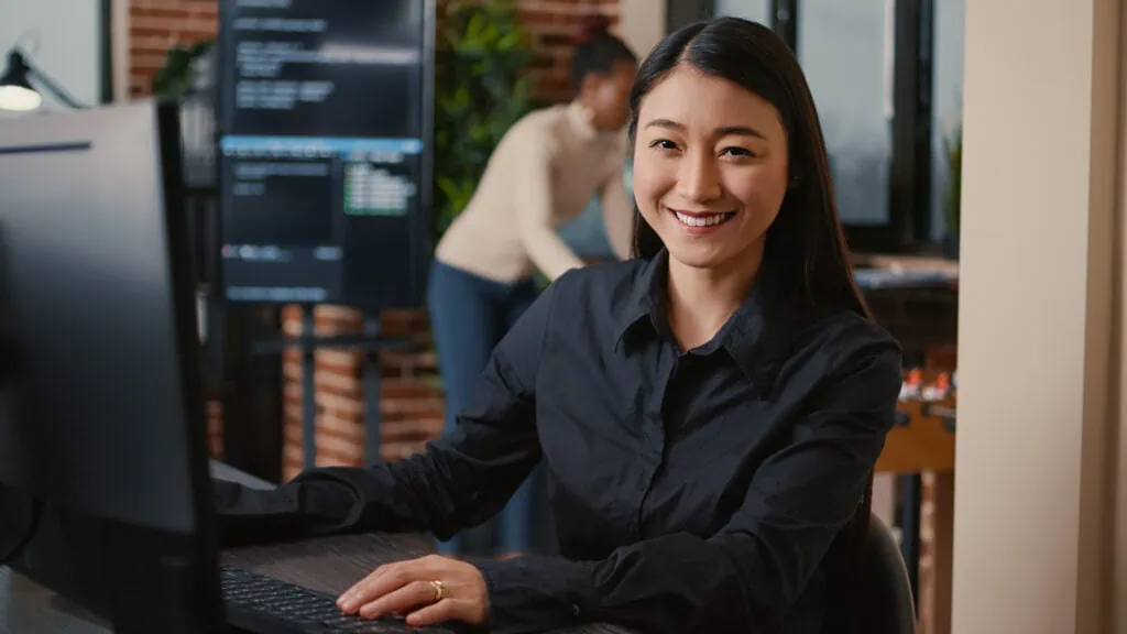 Die Softwareentwicklerin lächelt und setzt ihre Arbeit mit Amazon SageMaker fort. Sie tippt ML-Code auf ihrer Computertastatur ein, während sie an ihrem Schreibtisch im Big-Data-Büro sitzt.
