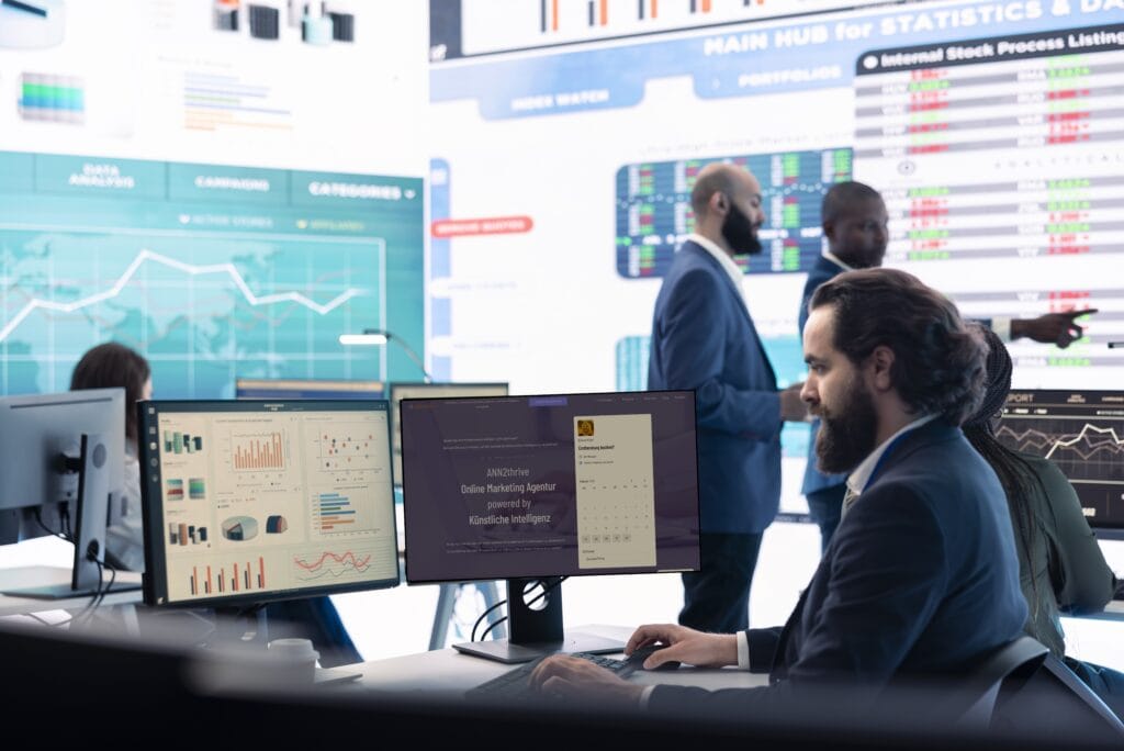 Ein modernes Büro mit mehreren Bildschirmen, die Marketing-Analytics-Dashboards und Finanzdaten anzeigen. Ein Mann in einem Anzug arbeitet konzentriert an einem Computer, während im Hintergrund Geschäftsgespräche stattfinden.