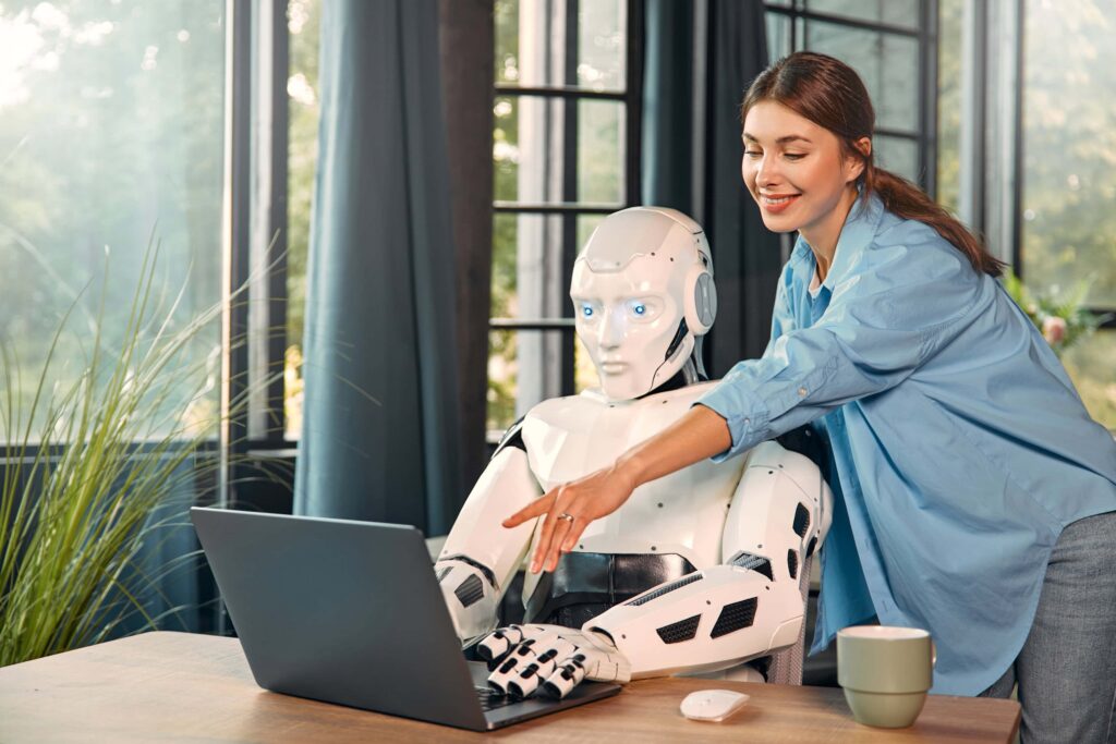 KI-Agenten oder ChatGPT: Eine junge Frau arbeitet mit einem humanoiden Roboter und einer Tasse Kaffee an einem Laptop in einem modernen Büro. Zusammenarbeit zwischen Menschen und künstlicher Intelligenz.
