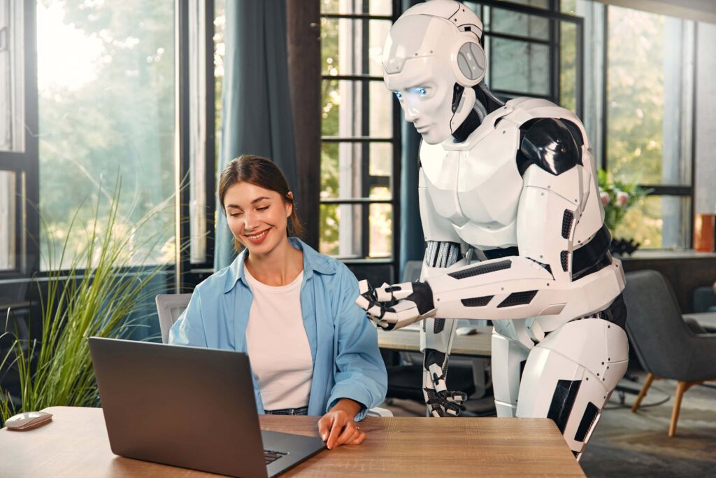 GPT vs. KI-Agententeam: Eine junge Frau und ein humanoider Roboter arbeiten gemeinsam an einem Laptop in einem modernen Büro. Eine Zusammenarbeit zwischen Mensch und künstlicher Intelligenz.