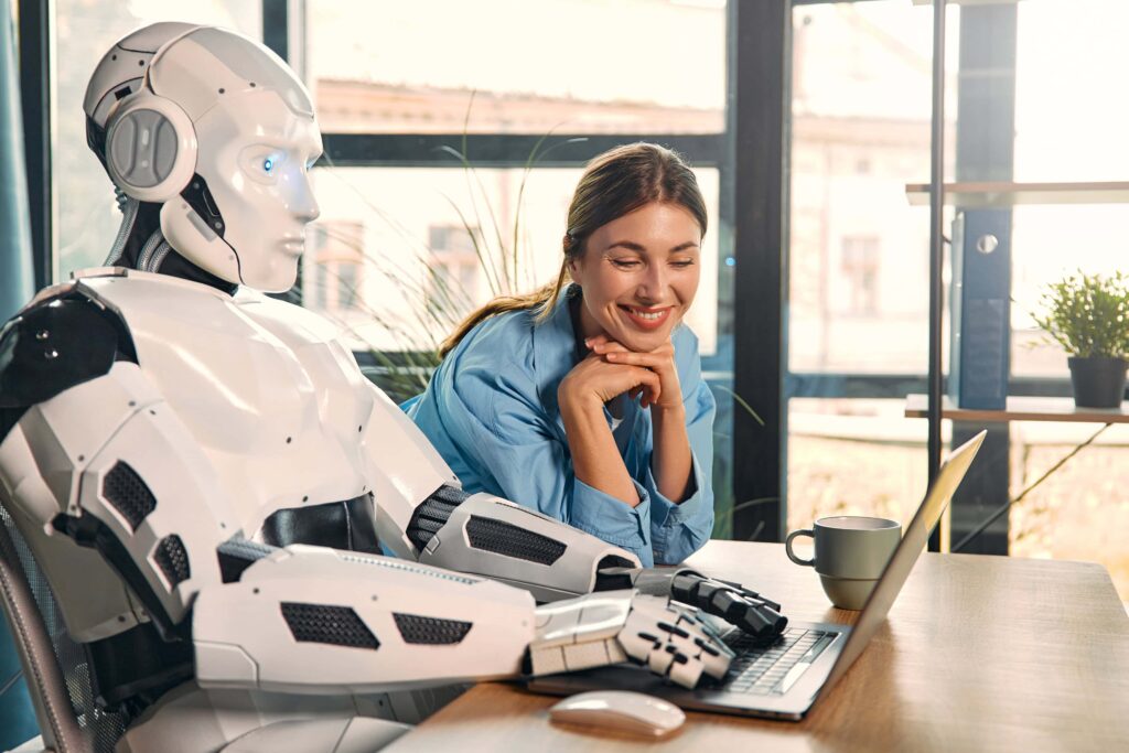 KI-Agententeam in der Praxis: Eine junge Frau arbeitet mit einem humanoiden Roboter an einem Laptop in einem modernen Büro und trinkt dabei Kaffee. Dies ist ein Beispiel für die Zusammenarbeit zwischen Menschen und künstlicher Intelligenz.